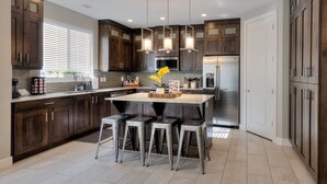 A modern kitchen with dark wood cabinets, stainless steel appliances, and a central island with bar stools. - Entrada 611 | 4BR Luxury Townhome, Pool, Hot Tub, Garage (Moab)