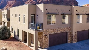 A modern two-story house with a balcony, stone accents, and a garage. - Entrada 611 | 4BR Luxury Townhome, Pool, Hot Tub, Garage (Moab)
