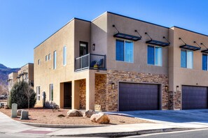 A modern two-story house with a stone facade, a balcony, and a garage. - Entrada 611 | 4BR Luxury Townhome, Pool, Hot Tub, Garage (Moab)