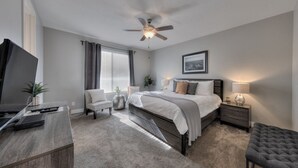 Une chambre moderne avec un lit, un bureau, une chaise, un téléviseur et un ventilateur de plafond.