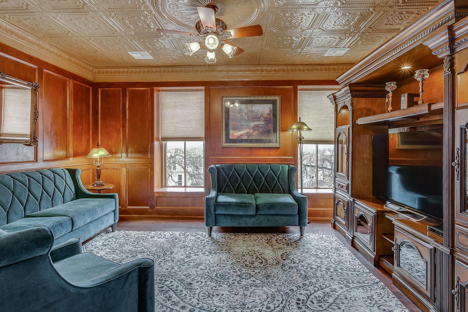 A room with a green sofa, a matching armchair, a large TV, and a patterned rug.