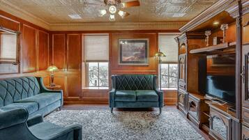 A room with a green sofa, a matching armchair, a large TV, and a patterned rug.