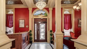 A grand hallway with red walls, a wooden reception desk, and a chandelier. - Historic Elgin Hotel (Marion)