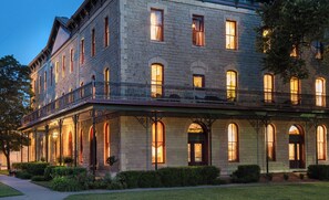 Un grand bâtiment en pierre, doté de nombreuses fenêtres et d’un balcon, entouré de haies bien entretenues et d’un sentier.