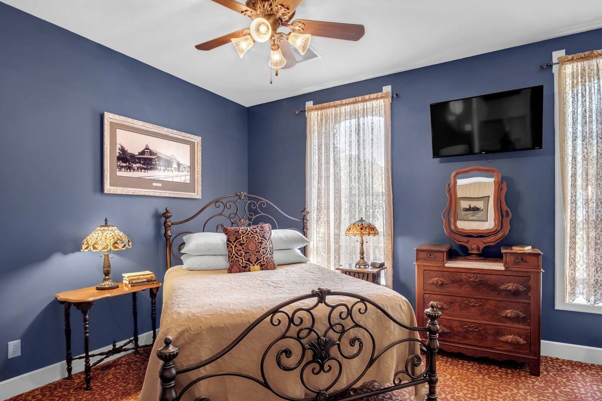 A bedroom with a bed, a dresser, a television, and a ceiling fan.