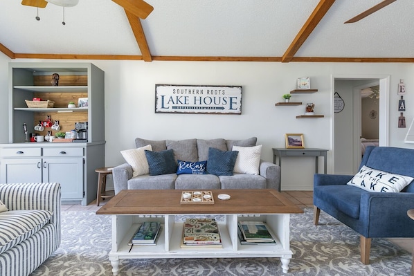 A living room with a sofa, coffee table, and a sign reading 'Southern Roots Lake House.' - Southern Roots Retreat: Spacious Home With Lake Views & Private Boat Launch (Downsville)