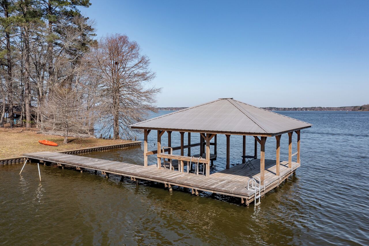 A wooden dock extending into a lake, with a covered pavilion structure at the end.