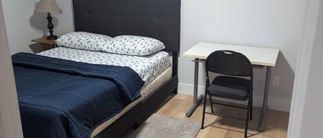 Une chambre à coucher comprenant un lit, un bureau, une chaise, une lampe et deux tableaux encadrés accrochés au mur.