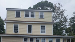 A two-story building with a garage, a covered porch, and a small front yard. - newly renovated studio is on the second floor. Pet friendly  and seven minute walk to the beach<br>- FREE parking<br>-ACs<br>- Pet friendly<br>- Queen bed<br>- Fast wifi<br>- Smart TV (Old Orchard Beach)