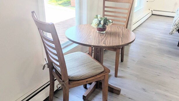 A dining area with a round table and two wooden chairs, a small vase with flowers, and a view of greenery outside. - newly renovated studio is on the second floor. Pet friendly  and seven minute walk to the beach<br>- FREE parking<br>-ACs<br>- Pet friendly<br>- Queen bed<br>- Fast wifi<br>- Smart TV (Old Orchard Beach)