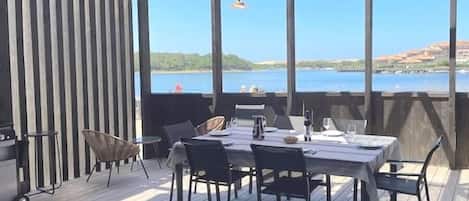 An outdoor dining area with a table set for four, surrounded by chairs, overlooking a body of water.