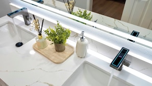 Une salle de bain moderne avec un lavabo en marbre blanc, un robinet numérique et un miroir doté d’une bande lumineuse.