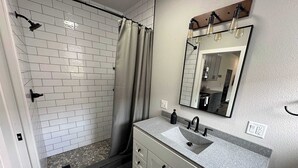A bathroom with a shower, a sink with a mirror, and a vanity with cabinets. - Downtown Minimalist Apartment (International Falls)