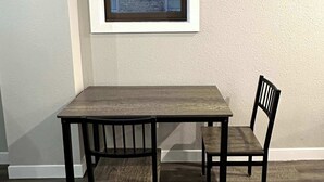 A dining area with a table and two chairs, a window with blinds, and a textured wall. - Downtown Minimalist Apartment (International Falls)