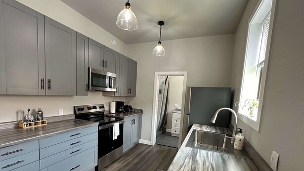 A modern kitchen with grey cabinets, stainless steel appliances, and a marble countertop. - Downtown Minimalist Apartment (International Falls)