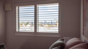 A bedroom with a window overlooking a cityscape.