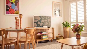 A cozy room with a wooden table and chairs, a bookshelf, and a window with blinds.