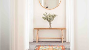 A hallway with a wooden bench, a round mirror, and a colorful rug.