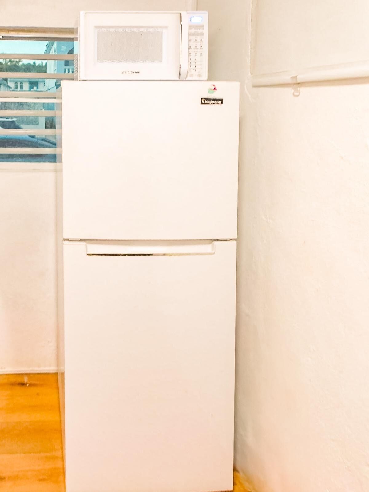 Ein weißer Kühlschrank mit eingebauter Mikrowelle, einem Magic Chef Logo und einem kleinen Fenster an der Tür.