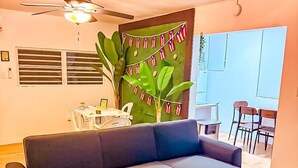 A modern living room with a sectional sofa, a ceiling fan, a large plant, and a view of the outside. - DtMF Experience at his Hometown in Vega Baja - Near Beach and Natural Springs! (Vega Baja)