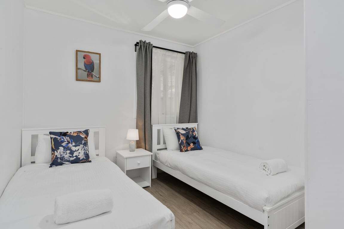 A twin room with two beds, a nightstand, a lamp, a ceiling fan, and a window with curtains.