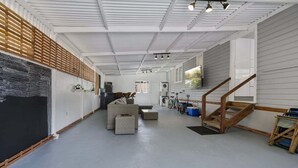 A spacious room with a high ceiling, a stone wall, and a wooden slat wall. There is a staircase leading to an upper level, and a bicycle is visible in the background.