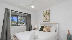 A bedroom with a large bed, a window with curtains, a bedside table with a lamp, and a painting on the wall.