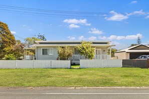 A single-story house with a front porch, a fenced yard, and a clear sky. - Pumicestone Porch – 4BR Pet-Friendly, Walk to Bongaree Jetty (City of Moreton Bay)