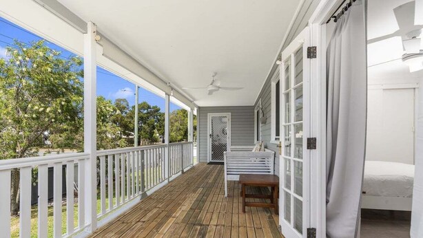 A covered porch with a wooden floor, white railings, and a bench.