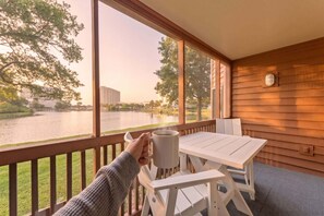 A wooden deck with a table and chairs, overlooking a body of water and buildings.