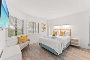 A bedroom with a bed, bench, bedside tables, and a wall-mounted TV.