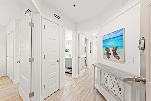 A hallway with white doors, a fireplace, and a beach-themed painting.