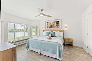 A bedroom with a bed, a ceiling fan, a bench, a bedside table, and a window with blinds.