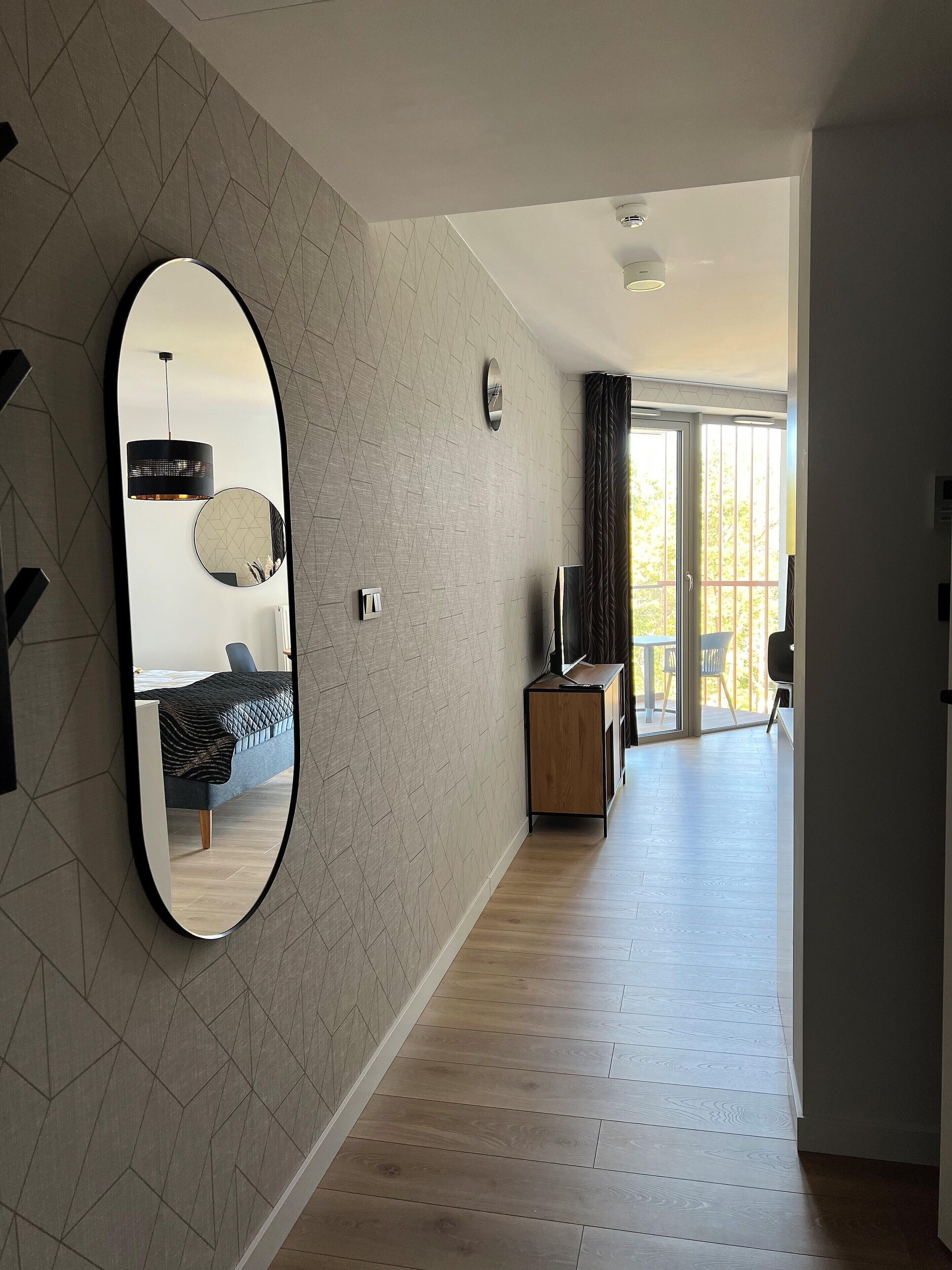 A modern living room with a large mirror, a sofa, a TV, and a wooden cabinet.