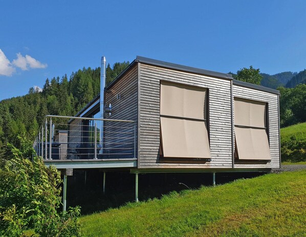 A modern cabin with a balcony, large windows, and a scenic mountain backdrop.