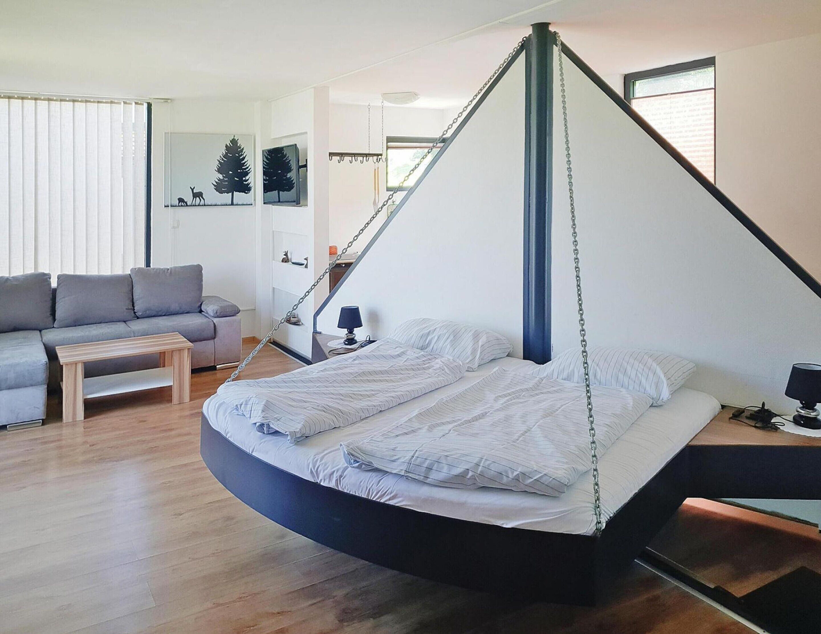 Un dormitorio tipo loft moderno con una cama colgante, un sofá gris y una mesa de centro de madera.