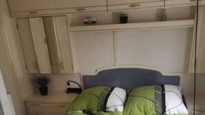 En snyggt bäddad säng med gröna och vita sängkläder, ett nattduksbord med en lampa och en liten växt på byrån.