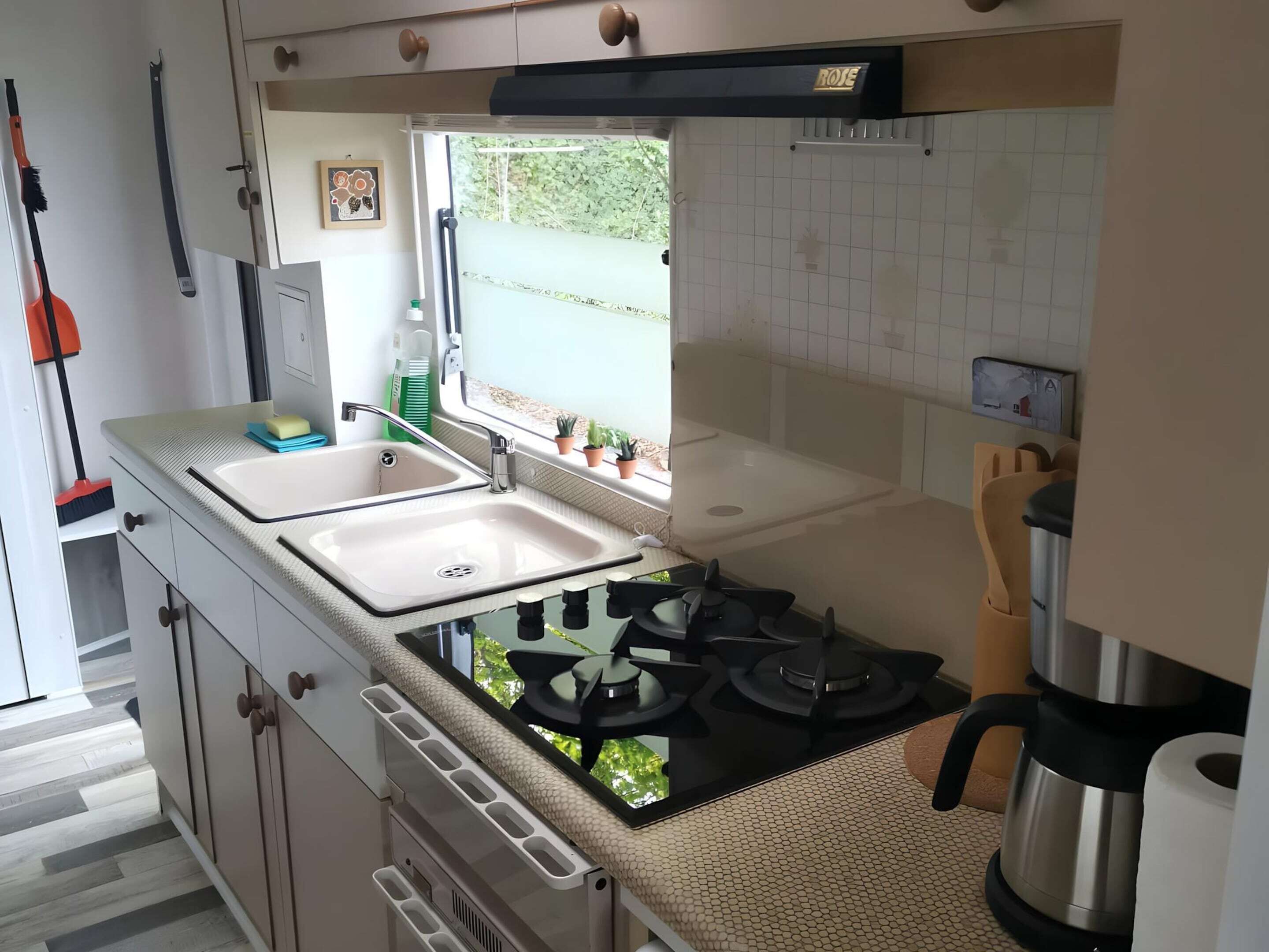 Una cucina compatta con piano cottura a gas, due lavelli e una finestra che offre vista sul verde.