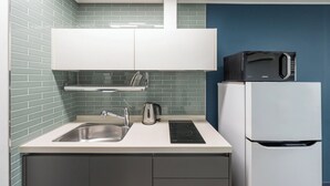 A modern kitchen with a stainless steel sink, kettle, and a microwave on top of a white refrigerator.