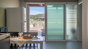 A room with a table, chairs, a sliding glass door leading to a balcony with a view of a green landscape.