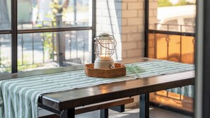 Una mesa con una cesta tejida que contiene un farol blanco, un mantel a rayas verdes y blancas, y una sola hoja verde.