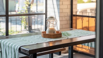Una mesa con una cesta tejida que contiene un farol blanco, un mantel a rayas verdes y blancas, y una sola hoja verde.