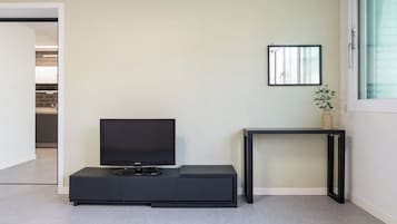 Una sala de estar moderna con un televisor de pantalla plana sobre un mueble negro, una mesita auxiliar con una planta y un cuadro en la pared.