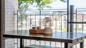 Una mesa con un farol y una cesta, frente a una barandilla de balcón con vistas a edificios y árboles.