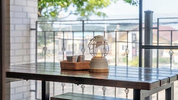 Una mesa con un farol y una cesta, frente a una barandilla de balcón con vistas a edificios y árboles.