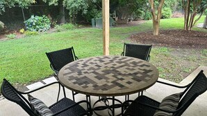 A round table with a checkered pattern, surrounded by four black wicker chairs with cushions.
