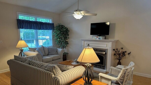 A living room with striped sofas, a fireplace, a television, and a ceiling fan.