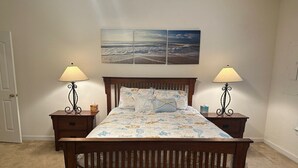 A bedroom with a wooden bed, two bedside tables with lamps, a wall-mounted picture, and a carpeted floor.