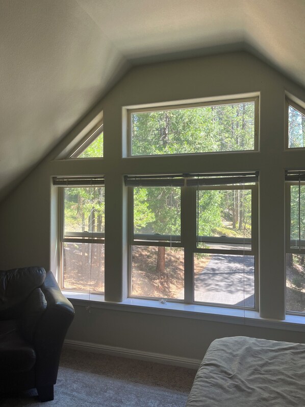 A bedroom with a sloped ceiling, a large window with multiple panes, a dark leather chair, and a bed with a white cover.