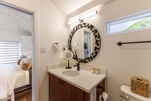 Un baño con un espejo redondo, un lavabo, un inodoro y una ventana.